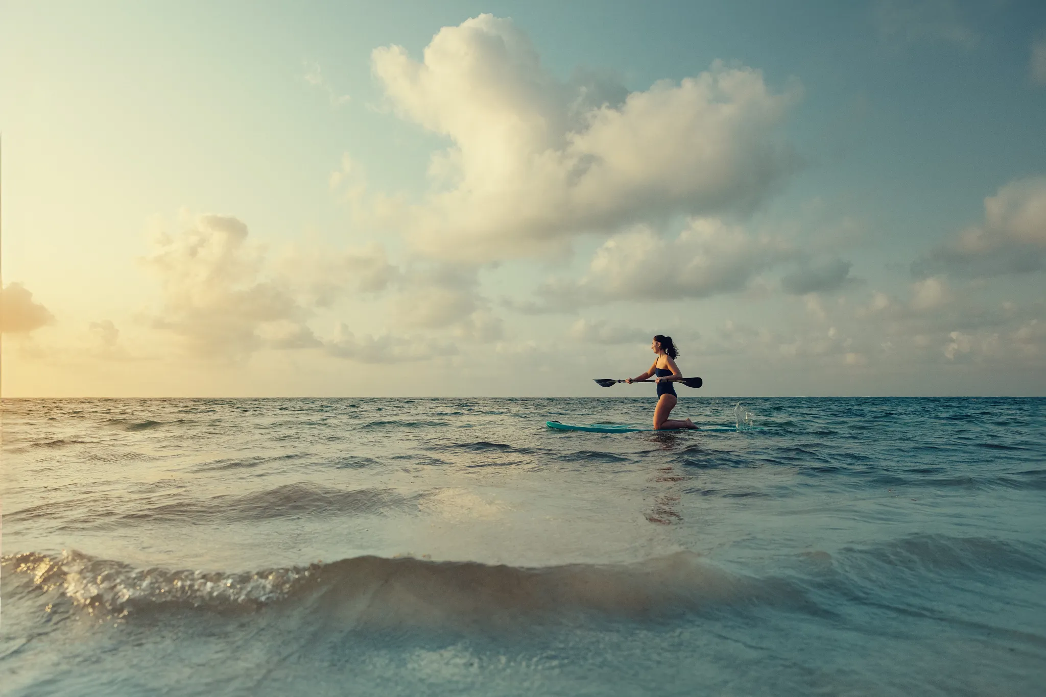 A woman paddleboarding on the ocean at sunrise at Breathless Riviera Cancun, an adults-only all-inclusive resort.
