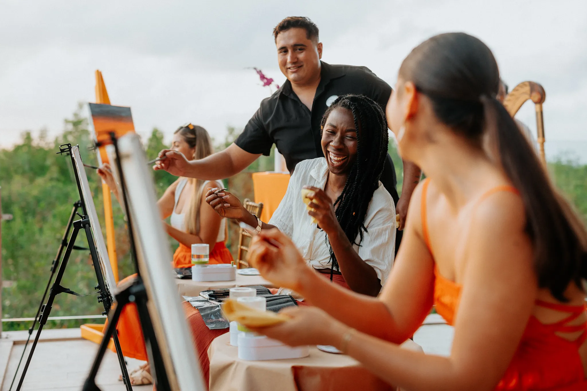 Friends enjoying a sip-and-paint activity outdoors, guided by a staff member.