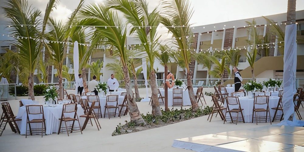 Pool area wedding reception setup with round tables, palm trees, and string lights at Dreams Onyx Resort & Spa