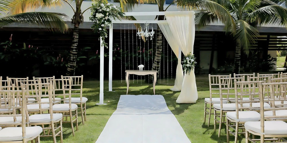 Tropical garden wedding ceremony setup with white arch, drapery, and palm trees at Dreams Onyx Resort & Spa