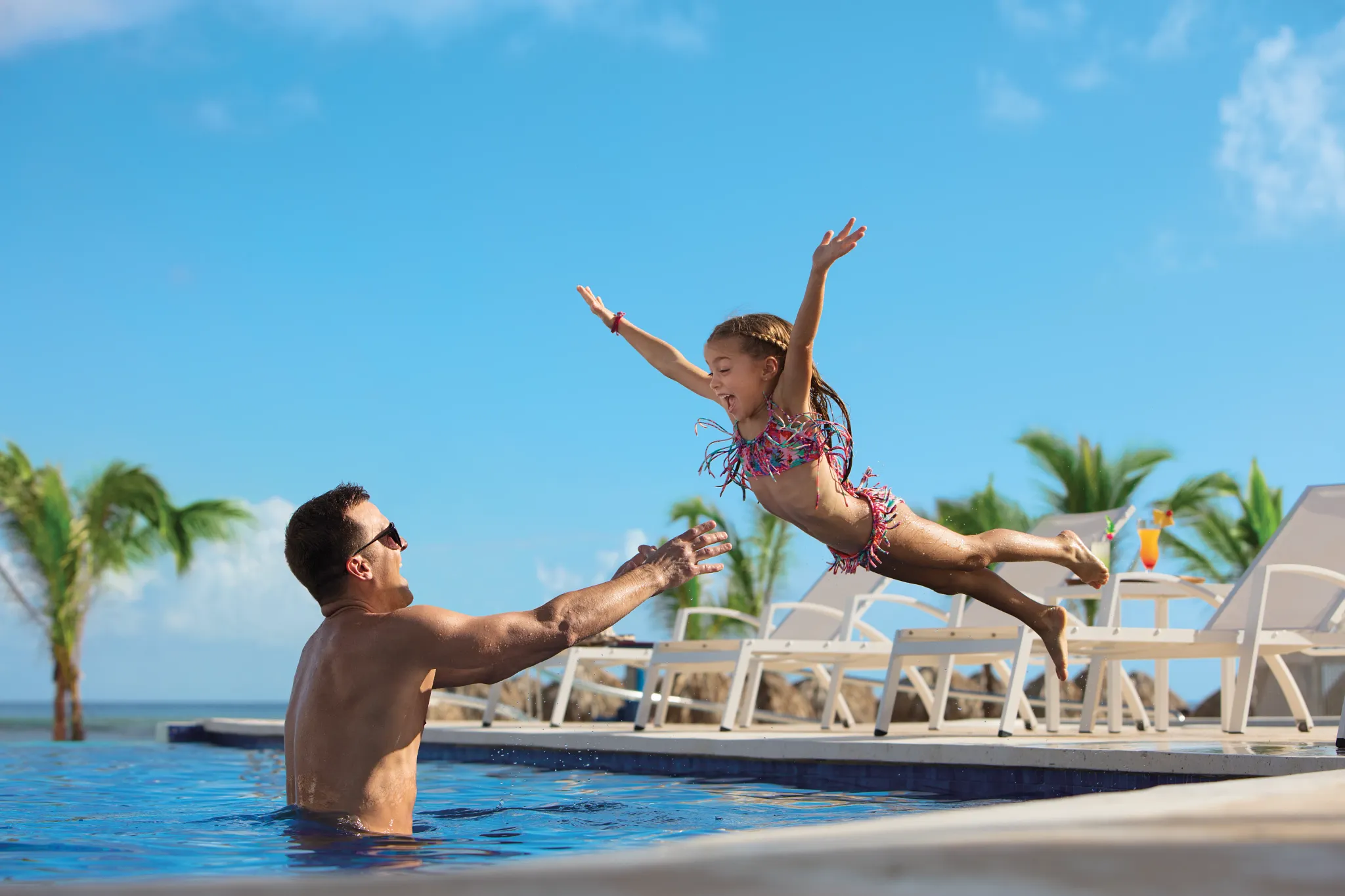Father catching his daughter mid-jump into a resort pool at Dreams Onyx Resort & Spa, highlighting fun family activities.